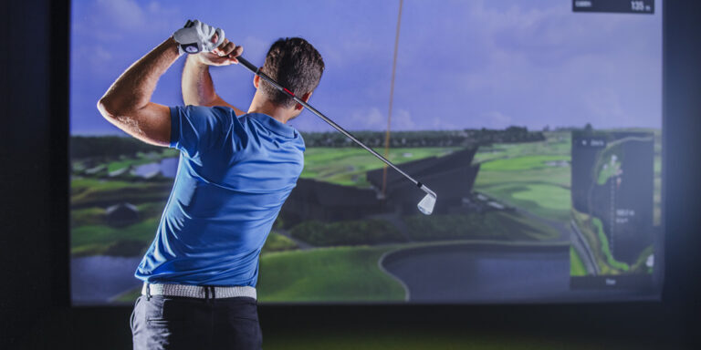 Golfer finishing a swing in a quiet simulator bay; dispersion chart on screen, notebook on table