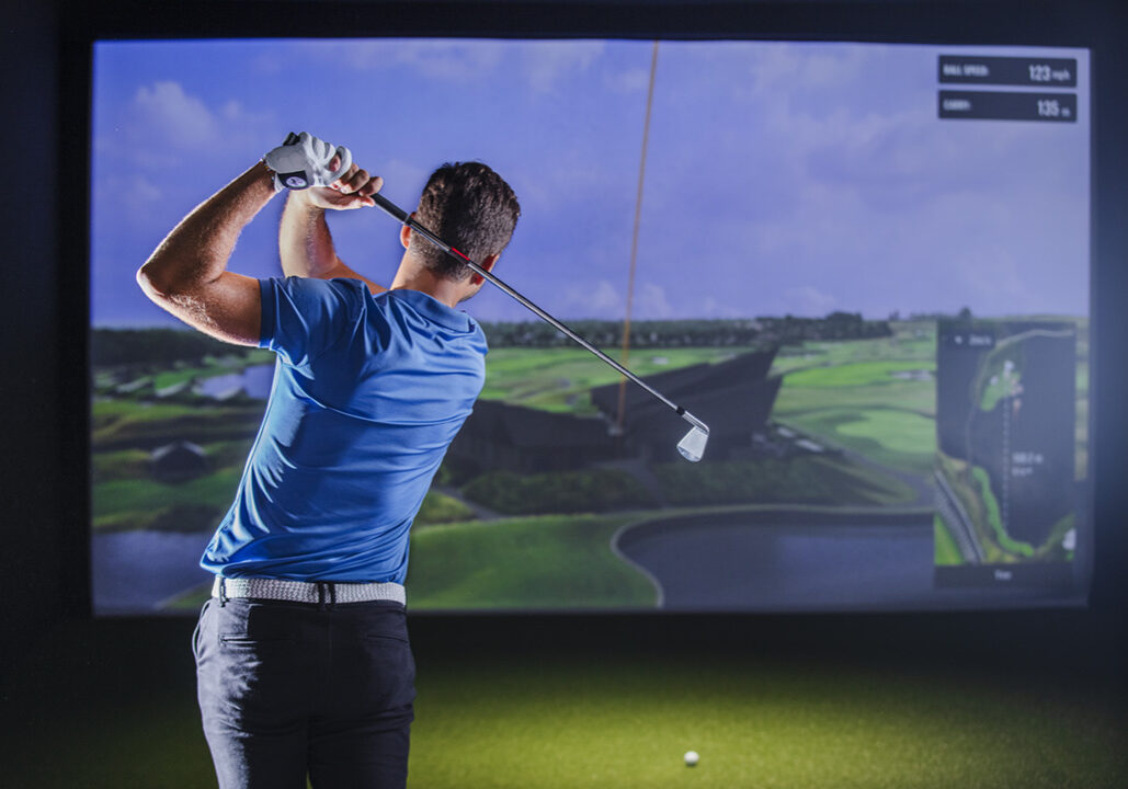 Golfer finishing a swing in a quiet simulator bay; dispersion chart on screen, notebook on table